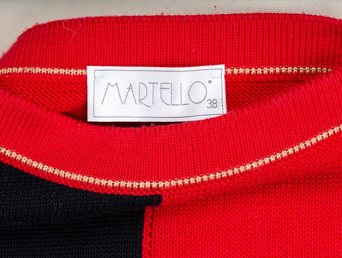 Genser. Rød genser. Foran 2 sorte felt, og 2 røde felt med gullfarget dekorasjon. 2 pynteknapper på hver skulder. Løstsittende genser.