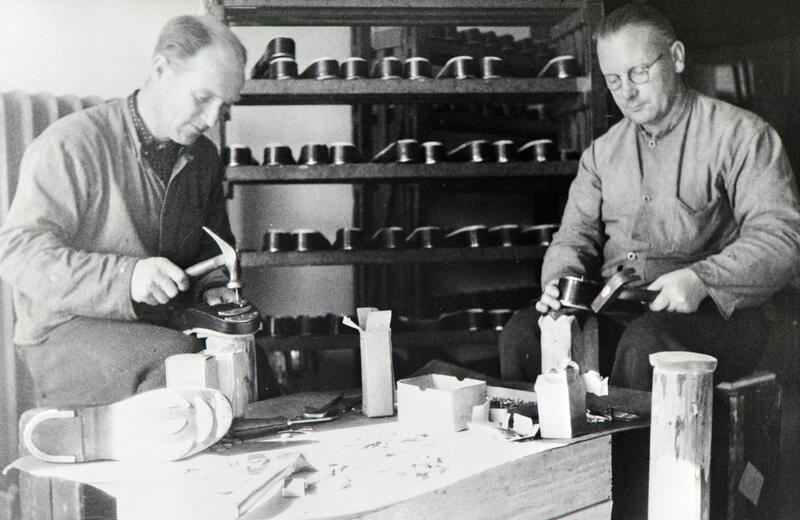 Svart-hvitt foto av to arbeidere ved Norrøna skofabrikk, som står og monterer hæljern på sko.