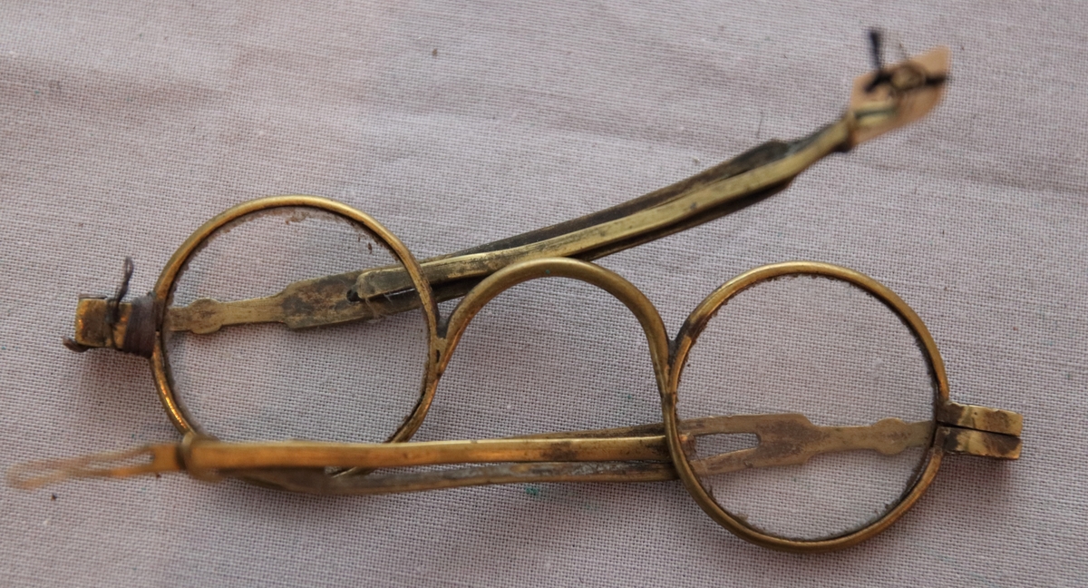 Glasögon med cirkelrunda glas. Ramar och skalmar av mässing, de senare med skjutbar förlängning, försedd med ögla.