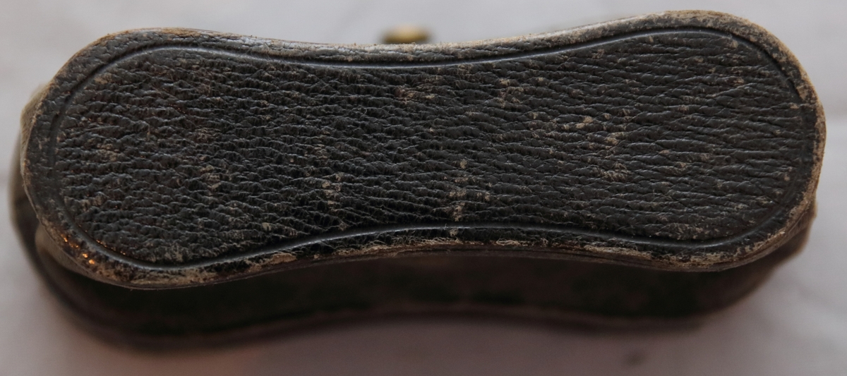 Kikare i fodral. Fodralet med stomme av trä täckt på utsidan av läder. Insidan av fodralet har lila tyg i lock och botten. Gångjärnen och låsmekanismen är gjorda i mässing. På utsidan av fodralet vid låsmekanismen sitter en knapp av mässing med en triangel med bokstaven "R" innuti omringat av strålar ut från triangeln. Fodralet har på insidan ett mönster/en bård målat i guldig färg. 
Kikaren är gjord i svartmålad mässing, glas pch metall samt är täckt av ett svart läder.
