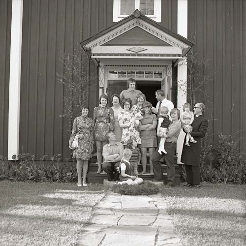 Lill-Annas dop sommaren 1973. Vuxna och barn samt präst har ställt sig på förstukvisten till gården Sunnanåker för en gruppbild.