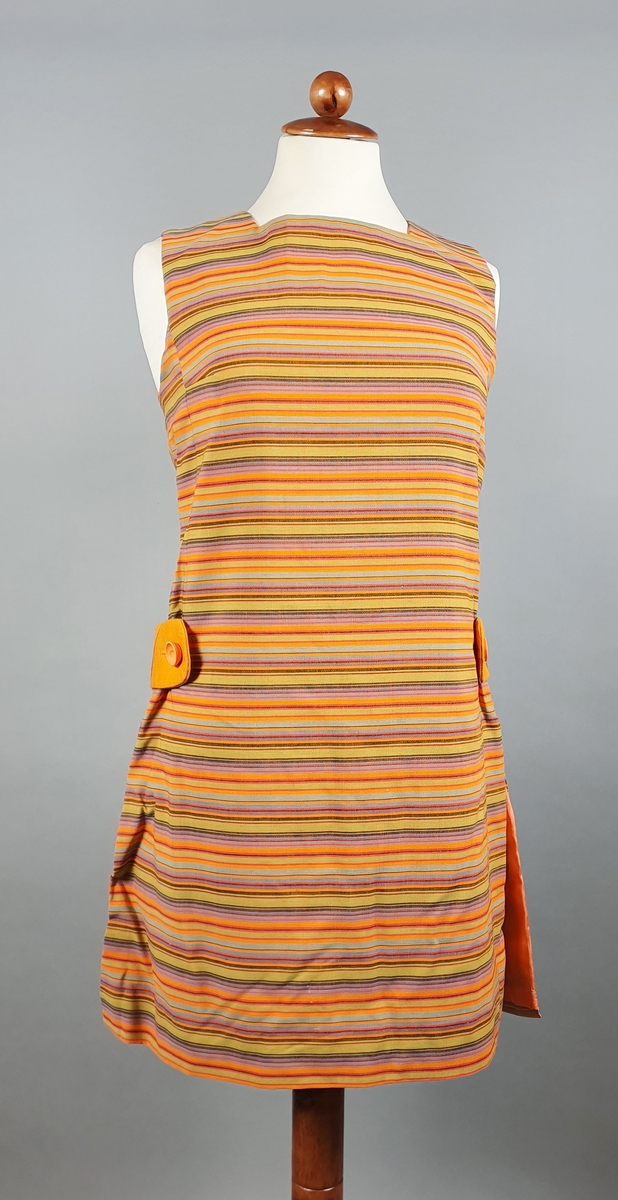 Tunika bestående av kjole og shorts (hotpants). Kjolen er uten ermer og har vertikale striper i oransje, grønt og brunt, med oransje belte (spensel) på ryggen med knapp som fester beltet på framsiden av hoften. Splitt i sidene.