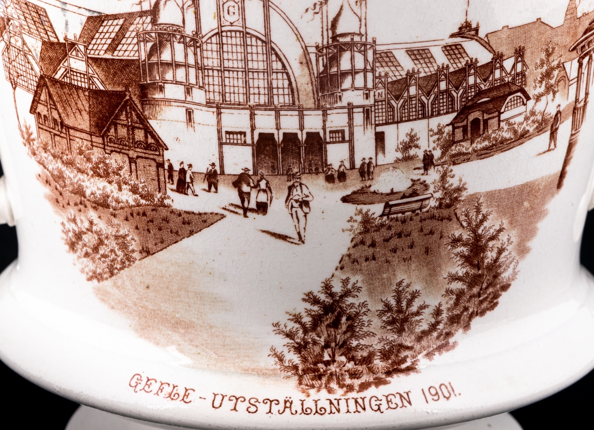 Blomkruka, "ytterkruka" tillverkad av flintgods av Gustavsbergsfabriken. Tillverkad som souvernir inför gävleutställningen 1901. Likartat motiv på två sidor i brunt koppartryck föreställande huvudingången till utställningen i Gävle.