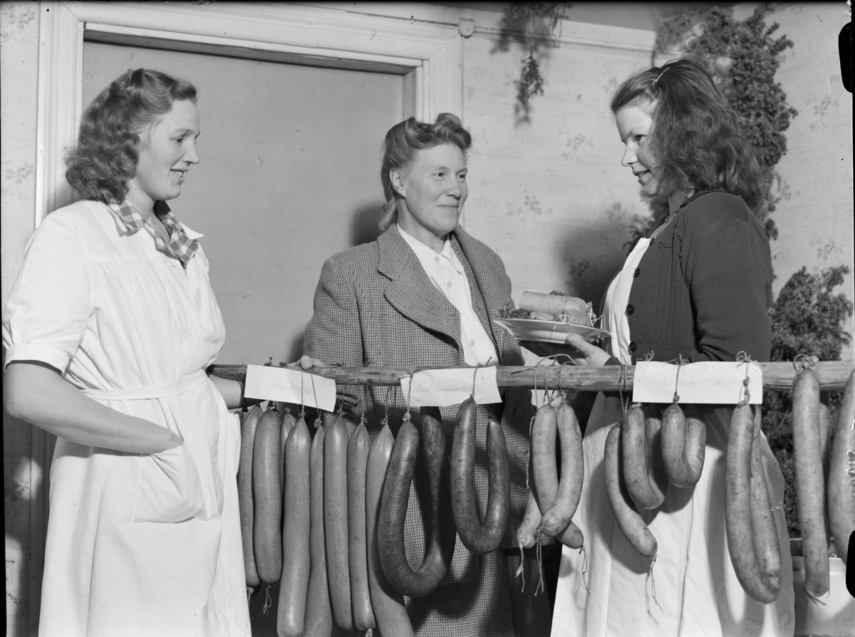 Kvinnor med olika sorters korv hängande på pinne, Uppland 1948