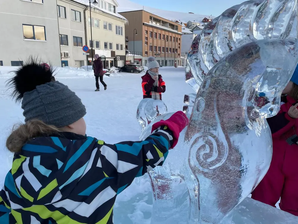 Et barn føler på en isskulptur av en hest.