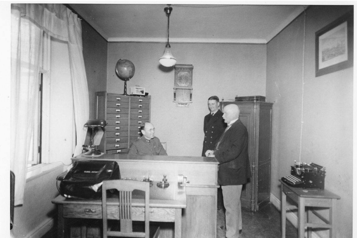 Interiör från arrestbyggnaden, övre våningen. Förvaltareexpeditionen. Fr. v. förvaltare Kindströmer, vaktmästare Fransson, skräddarmästare Friström. Marieberg juni 1937.