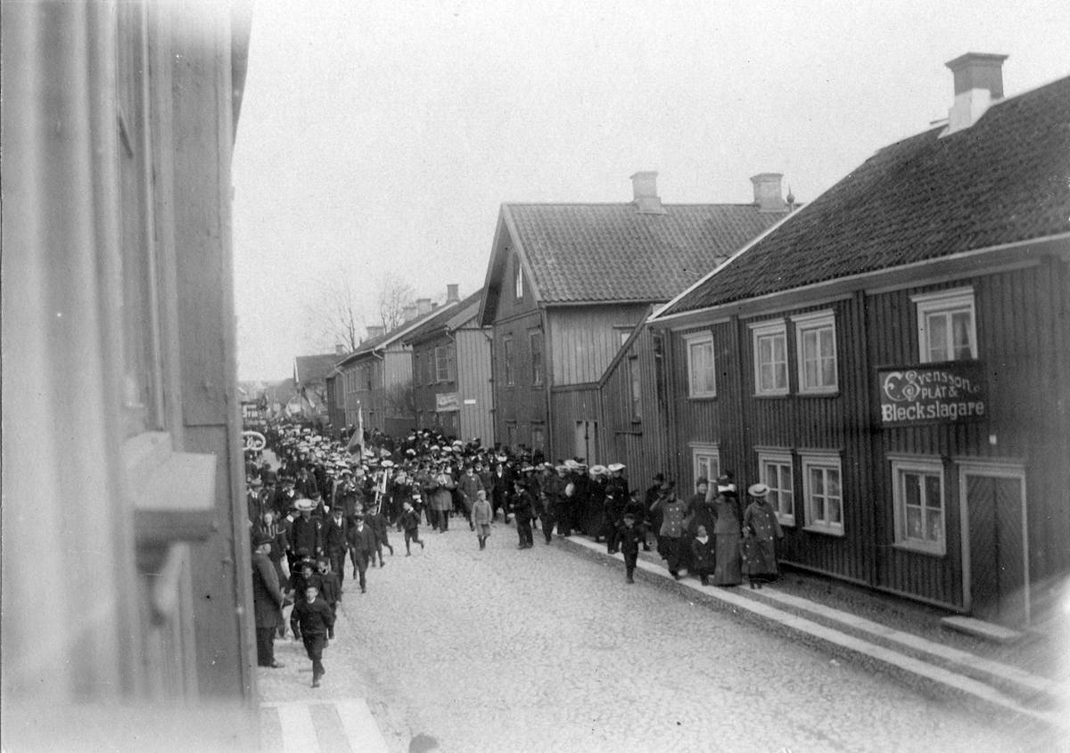 Första maj-tåg vid kvarteret Friden, Drottninggatan mellan Färgaregatan och Torggatan. Fastigheten riven 1910.

På fasaden hänger en skylt för "E. Svensson plåt- och bleckslagare".