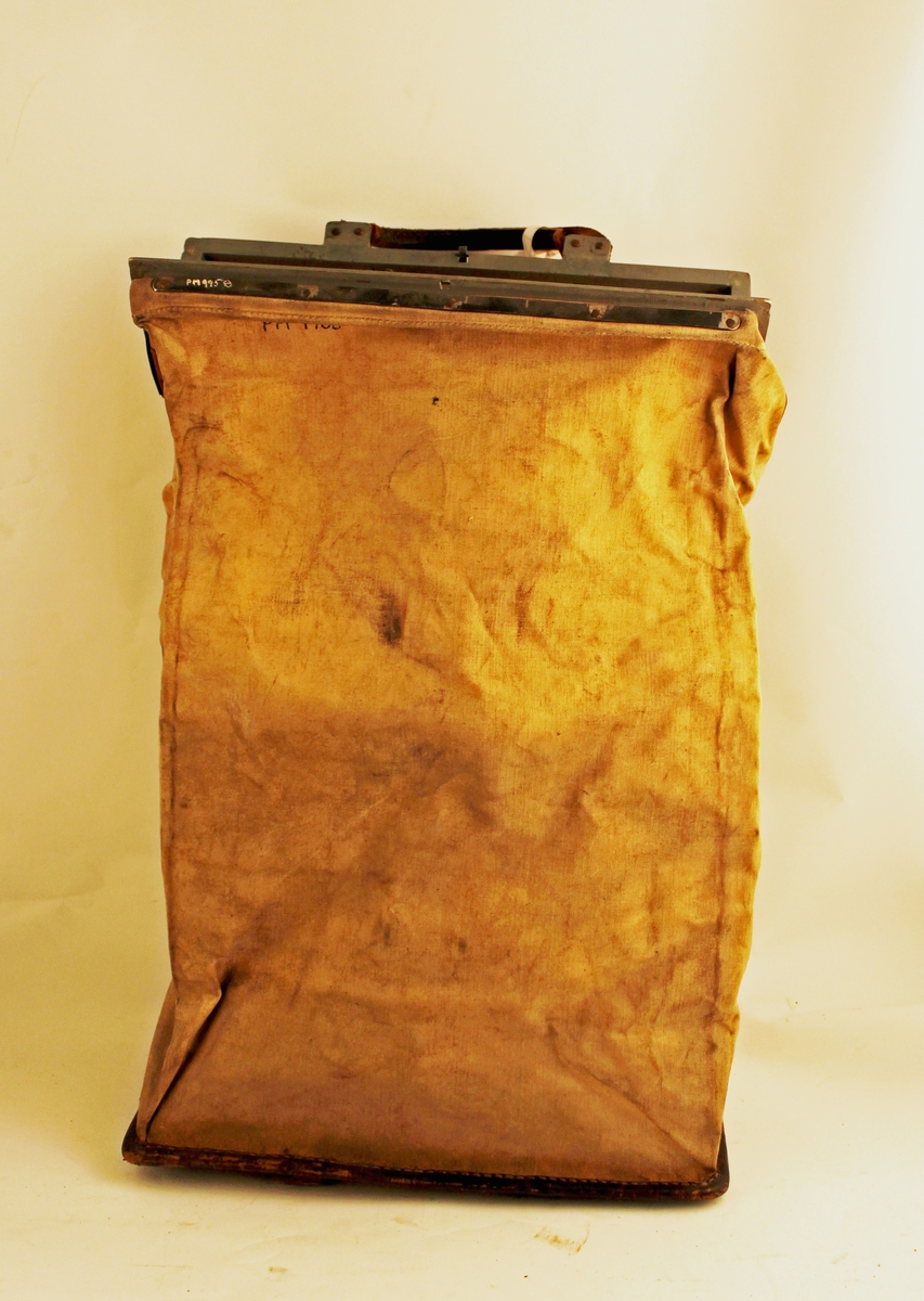 Tömningsväska av säckväv med järnarm (låsten) och läderskoning på den flata bottnen. Läderhandtag på ramen och bottnen gör att väskan kan bäras dubbelvikt.