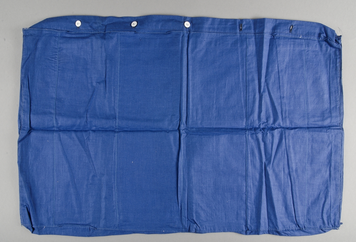 Madrassfodral av blått bomullstyg, maskinsytt med handsydda knapphål. På insidan fack där madrassstoppningen skulle placeras. Knäpps med fem linneklädda knappar.