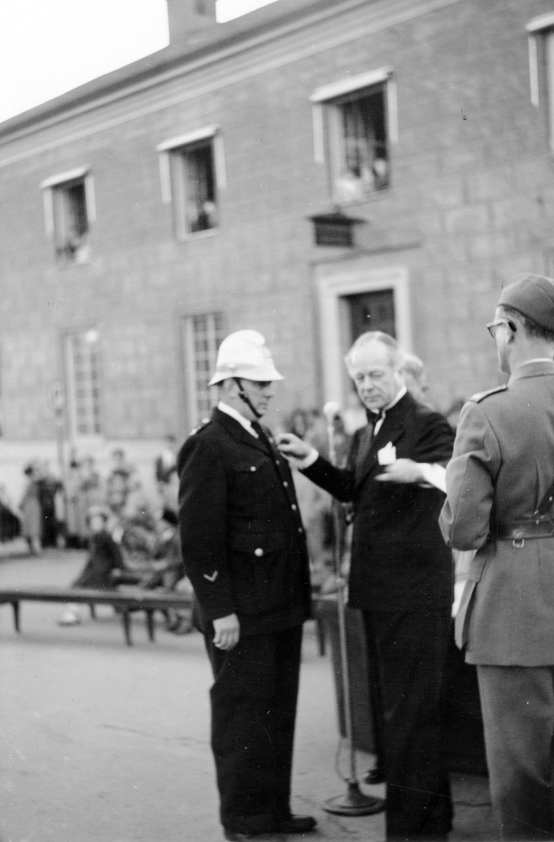 Brandkårens 50-årsjubileum 1950. Tre män i förgrunden, Landshövding A. Richert överlämnar medaljer till brandman.