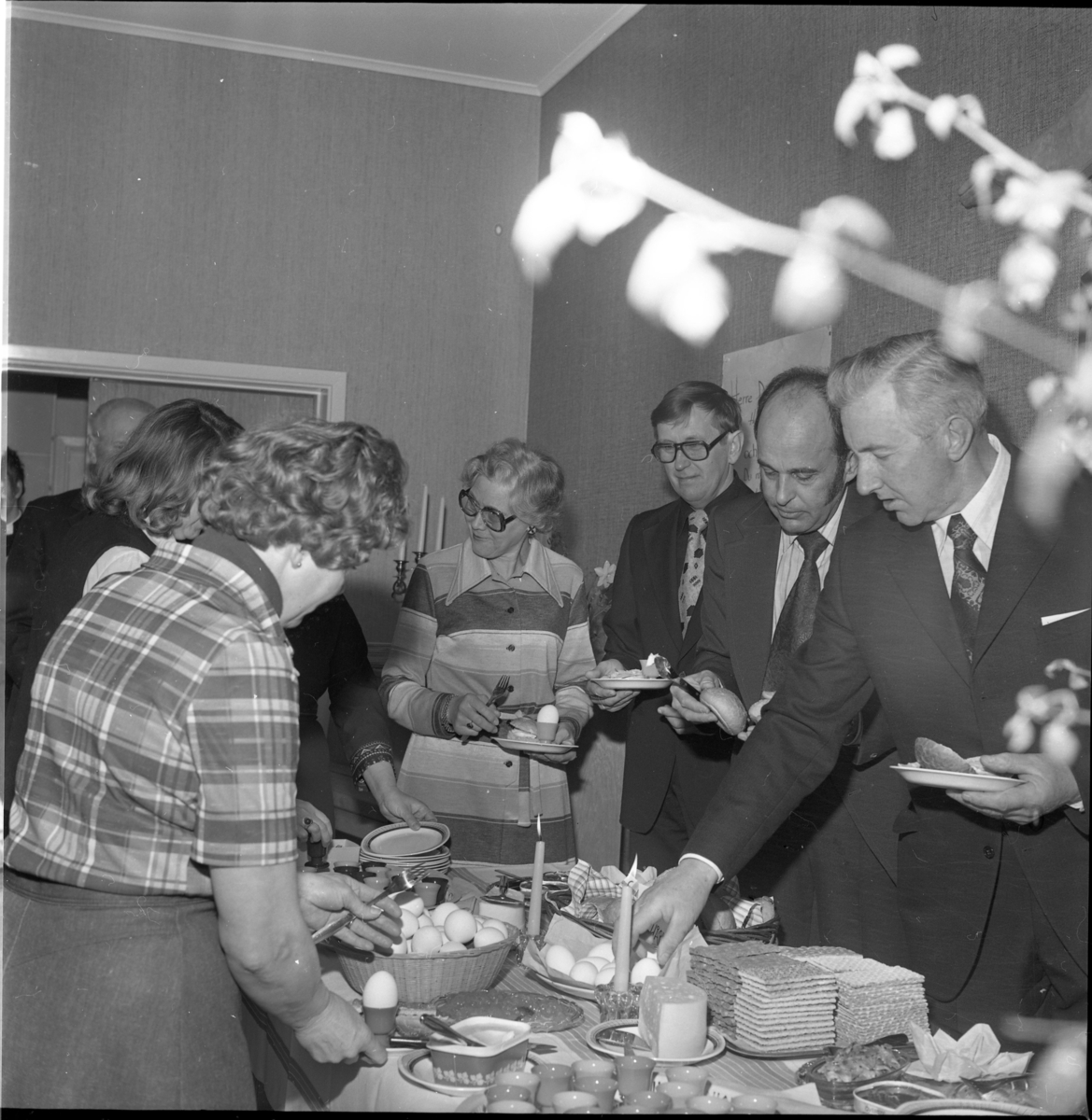 Män och kvinnor plockar från ett uppdukat frukostbord. Det är Ölmstad kyrka som bjuder på påskfrukost. Kvinnan i mitten med glasögon är Birgit Heldebrandt, fotografens hustru. Från höger står Robert Gustafsson, kantor Curt Malmberg och Lennart Fritsell.