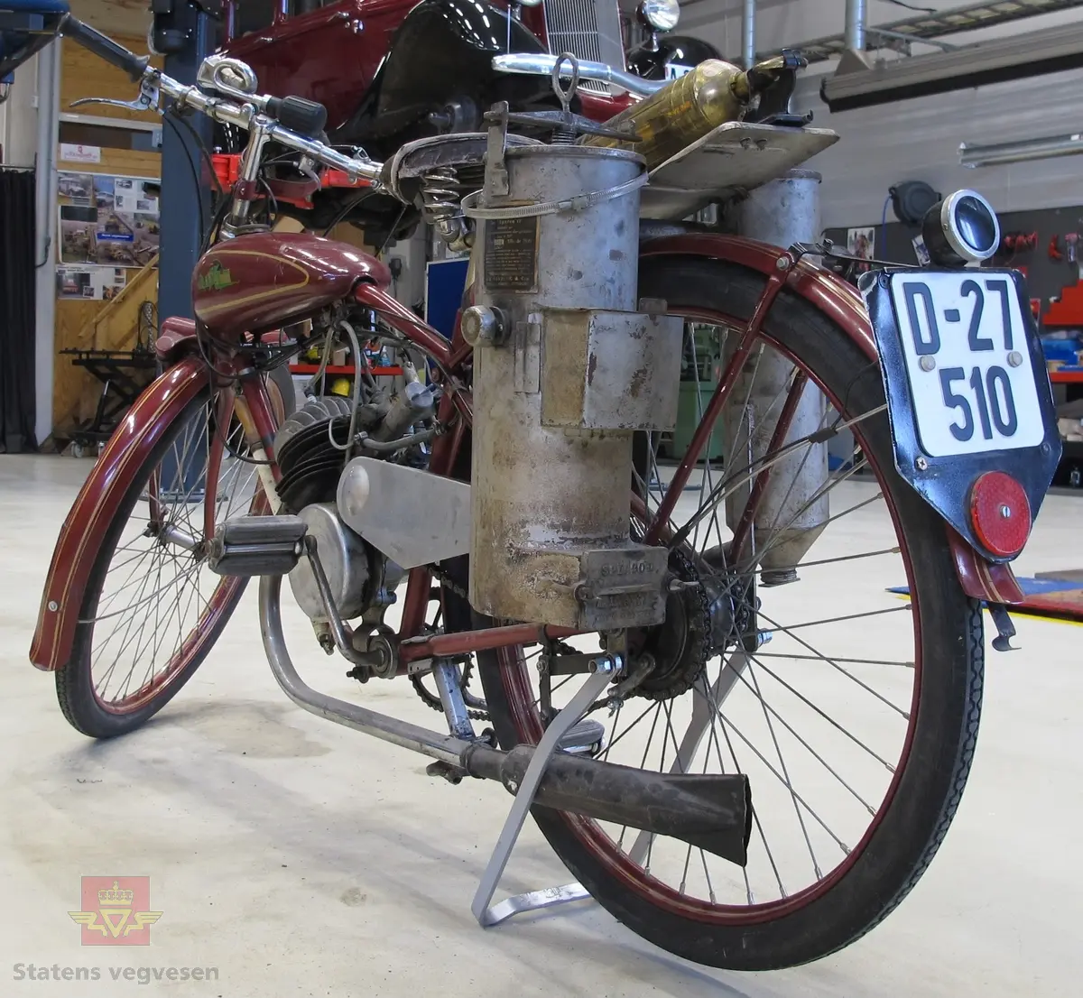 Blixt 98 cm3. Rød (vinrød), motorsykkel med pedaler, forbrenningsmotor og vedgassgenerator. 
Motorsykkelen er en BLIXT lettvekts motorsykkel fra 1936 med en 98 cc, en-sylindret totaktsmotor av fabrikat Fichtel & Sachs som yter 2,5 hk og går på bensin.
Generatoren er av fabrikat Åsbrink, type Sperco lI, og laget primært for bruk med trekull. Virkningsgraden er ca 0,4 med "godt køl", det vil si en 2,5 hk motor kan under gunstige omstendigheter teoretisk utvikle ca 1 hk. Kullet skal knuses til biter av størrelse 5-15 millimeter, og oppfyringen er svært omstendelig. I teorien skal man kunne kjøre ca 10 km på "en fyring".
Motorsykkelen har 2 gir og veier 73 kilo.
Den er 72 cm bred, 210 cm lang, og ...høy...
På hele sykkelen er det 1 sitteplass.
Det er montert pumpe til dekkene på ramma og et brannslukkingsapparat bak på sykkelen.