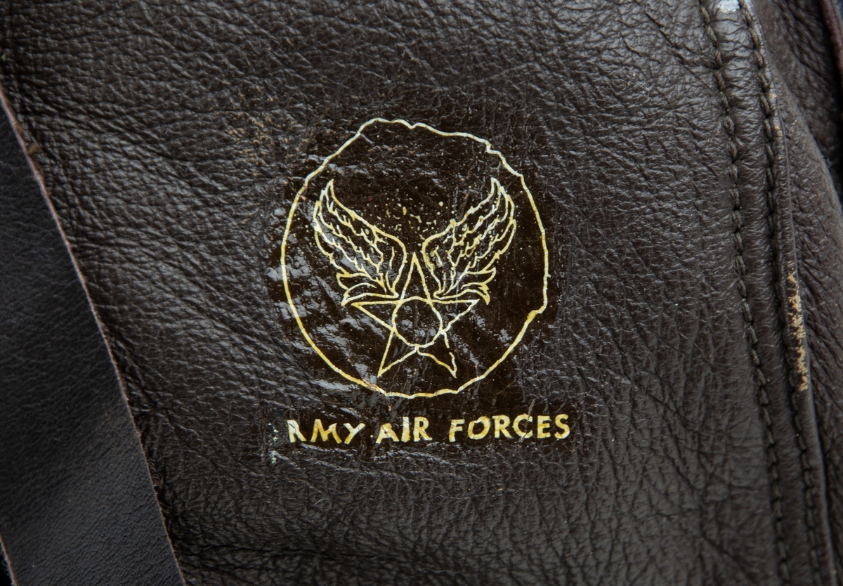 Flyghuva utförd i brunt skinn, typ A-11. Storlek medium. Motiv i nacken i form av cirkel innehållande stjärna med vingar samt nedanför text "Army air forces". Insida finns påsydd textil etikett