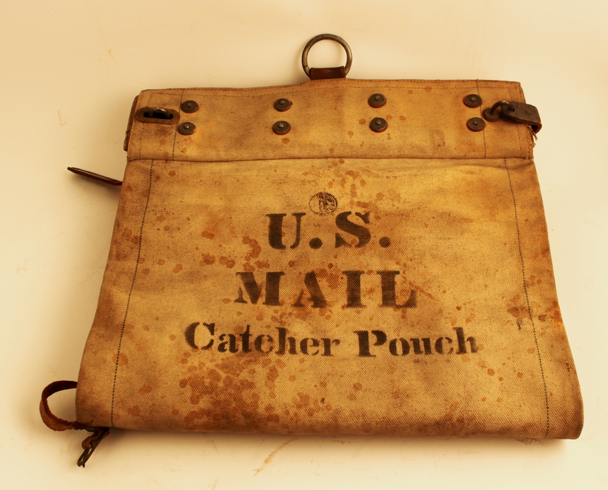 Postsäck av grå väv, med låsinrättning upptill av järn och mässing. En läderrem spändes runt öppningen och låstes. Säckens botten är av brunt läder och cirkulär. Säckens båda ändar försedda med järnringar som handtag eller upphängningsanordning. Säcken bärtexten "U.S. MAIL CATCHER POUCH" vilket antyder att säcken kanske fångats upp i farten, kanske av postkupér.