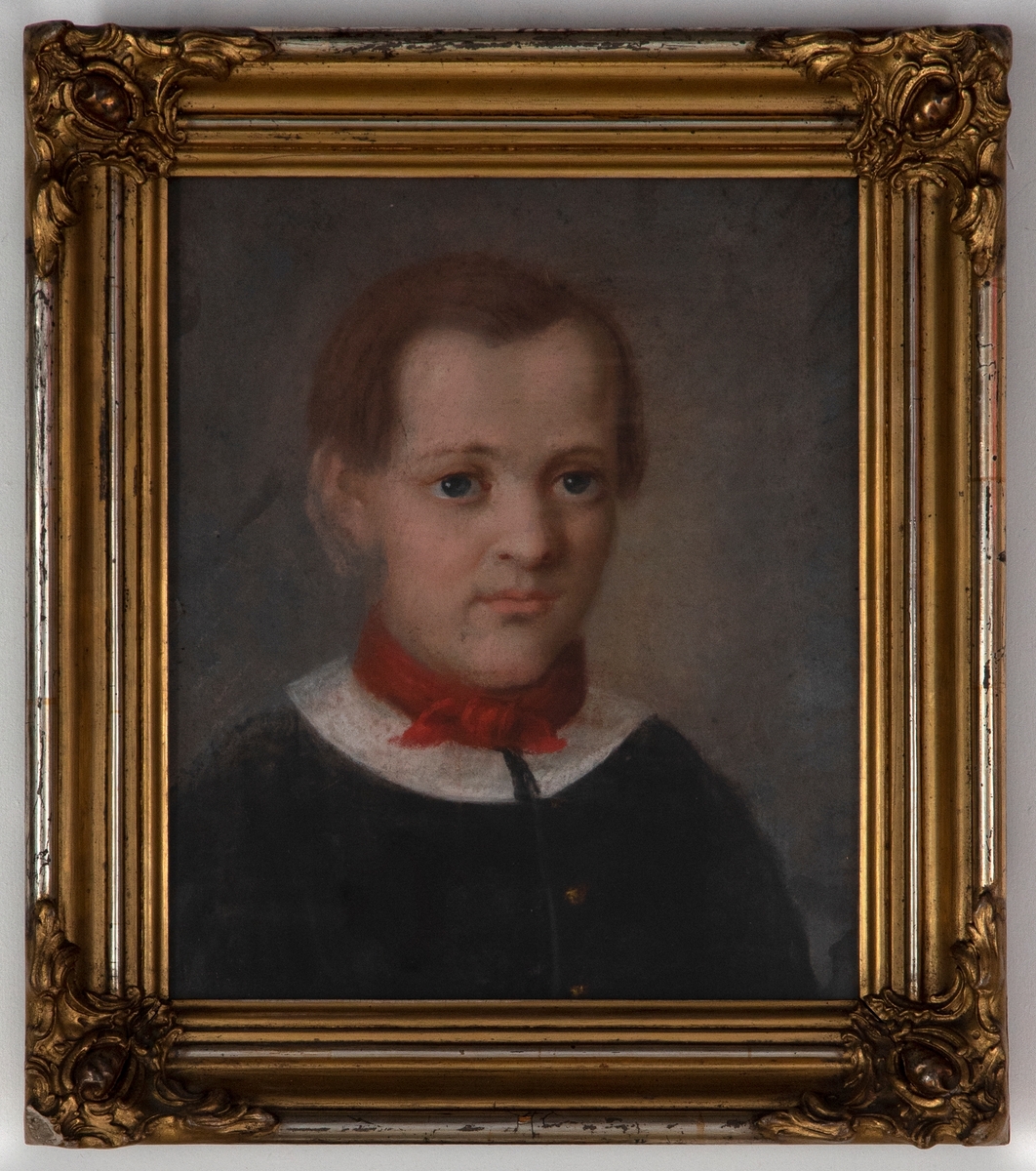 Portrett av en gutt med mellomblondt hår og blå øyne på grålig bunn. Gutten er iført en enkeltspennet mørk jakke med rund hvit krage og et rødt tørkle rundt halsen.