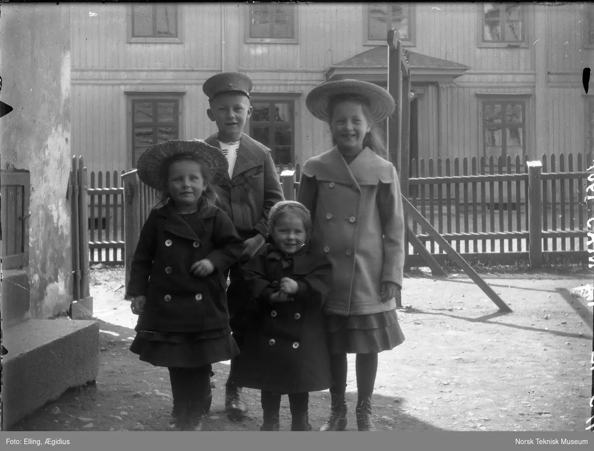 Barn, tre piker og en gutt i sin fineste utestas fotografert i haven oppstilt foran stakittgjerde : muligens Ægidius Ellings døtre i forgrunnen