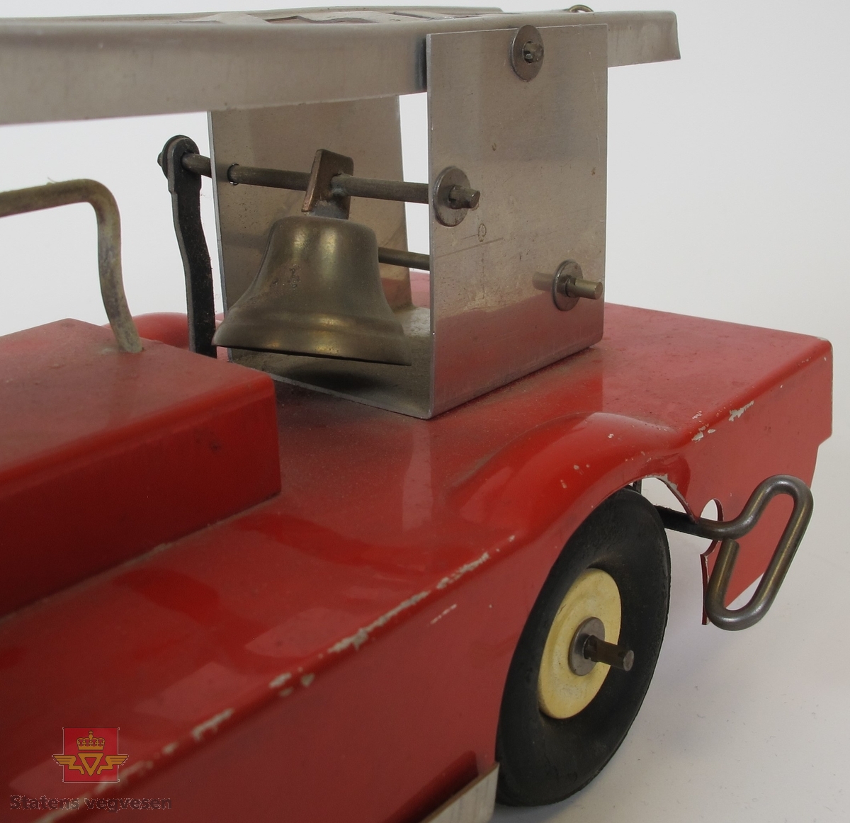 Opptrekkbar lekebil (brannbil) med stige som kan heves og senkes med eget sveive-håndtak. Laget hovedsakelig av metall. Opptrekkeren er koblet til bakhjulene og er en form for fremdrift. Bjellen over bakhjulene klirrer når hjulene er i bevegelse.