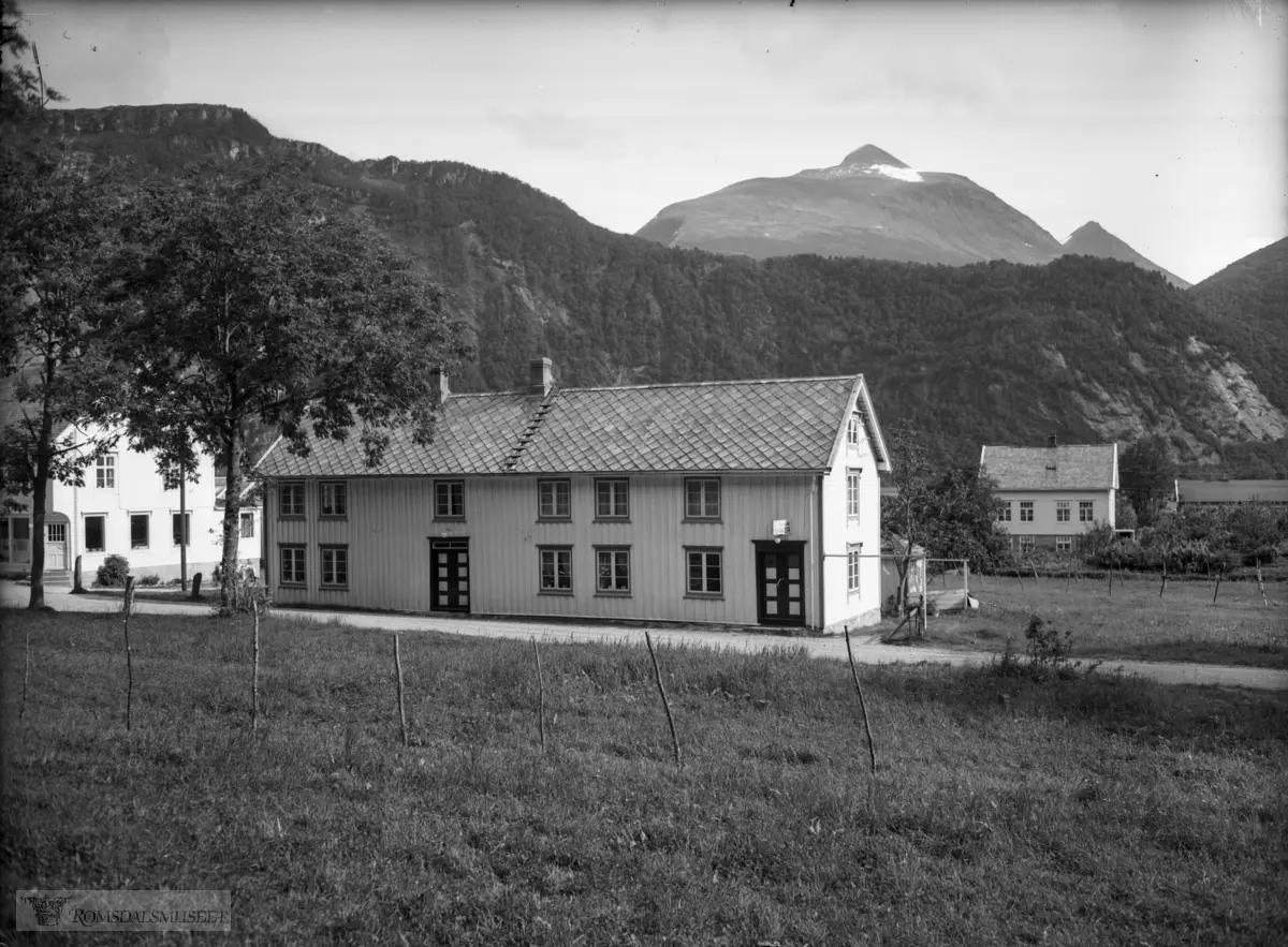Baker P. Ranvik..Nauste, Eresfjorden med Skjorta i bakgrunnen. Huset t.v. er Eresfjord Handelslag (bygd 1929), Kremmerbukta, gnr. 93/12 der bakar Peder Ranvik heldt til, og den neste huset er gnr. 93/39 Strandheim – Gyldenskoghuset.