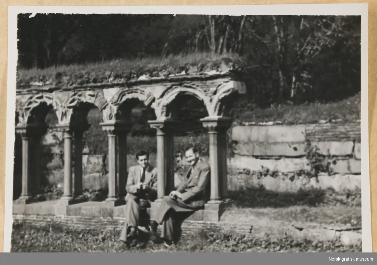 Utendørsmotiv. To menn i dress og slips sitter under søylegang. Fra Lysekloster. Fotografert i forbindelse med Vestlandsk Trykkerstevne i Bergen, 1946.