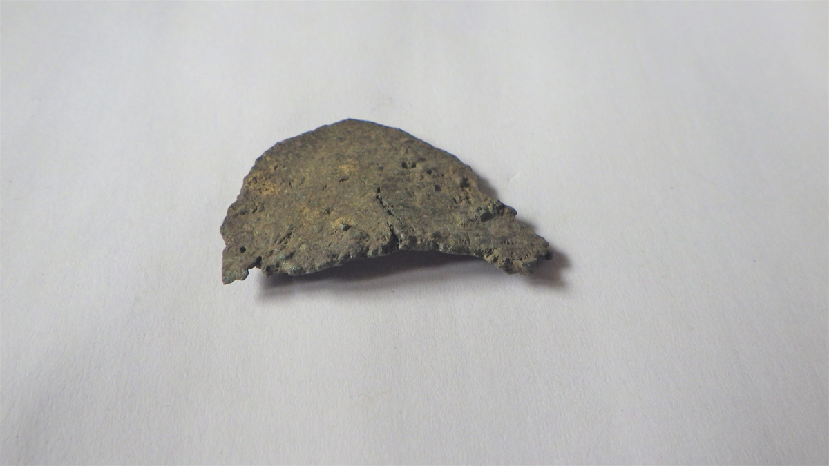 En stk metallplate med svært slitt oveflate og svakt buet fasong. Gjenstanden er trolig verkstedsavfall. 
