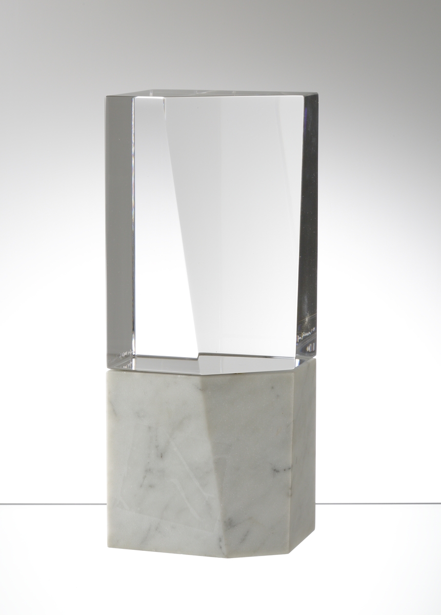 Formgiven av Jan Johansson. Rektangulär stående form med ett plan slipat i vinkel. Sockel i marmor som följer glasets form och som tillsammans med detta skapar en enhet.

Obs 2 delar.