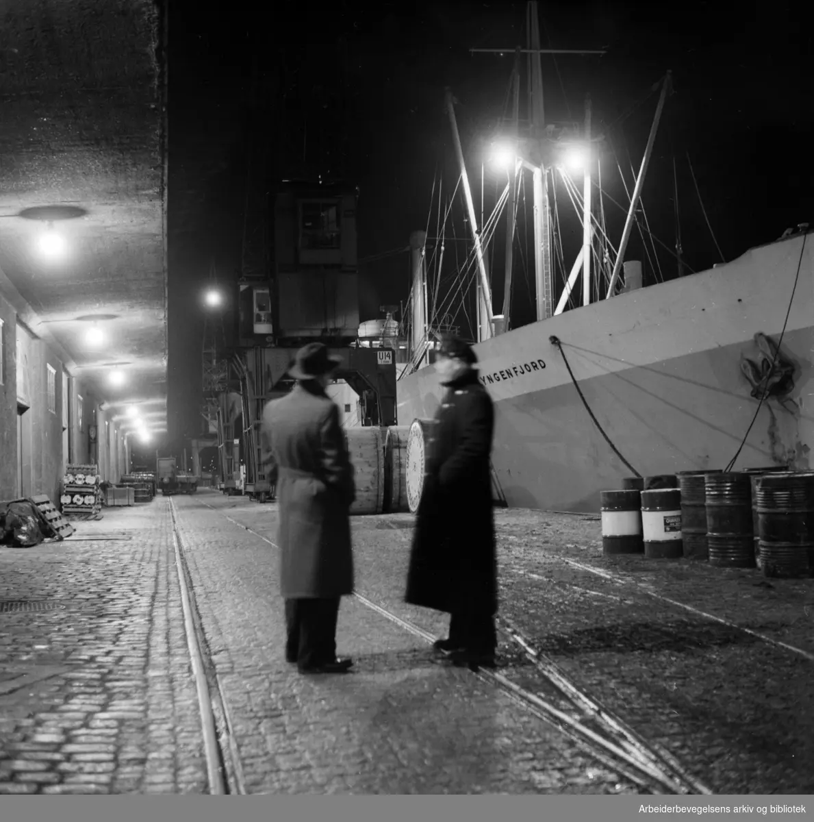 "Hard sno og kaldt for tollerne som gikk vakt på Amerikalinjens kai i går kveld". M/S Lyngenfjord til høyre på bildet. Januar 1954