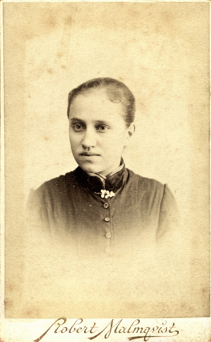 Ateljéporträtt av en okänd ung kvinna med brosch på halskragen. Troligen fotograferad i Halmstad.