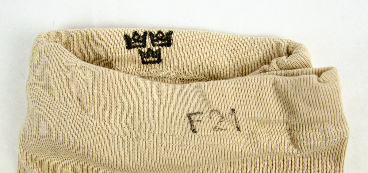 Underställsbyxa utförd i oblekt bomullstrikå. På insidan av byxlinningen finns maskingjord etikett "storl 5.", samt stämplat motiv i svart bläck iform av tre kronor. På byxlinningens utsida finns i svart bläck stämplat "F21"