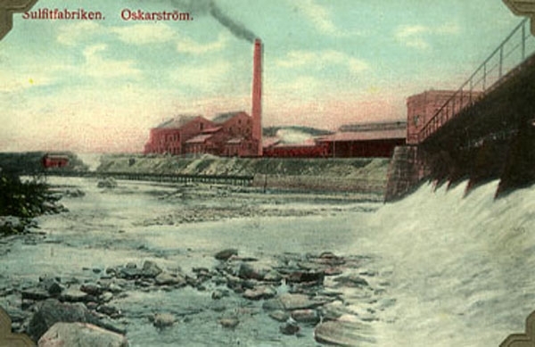 Handkolorerat vykort, "Sulfitfabriken. Oskarström." Fördämningen ligger till höger i bild och bortom den breder fabriksanläggningen ut sig med en hög, rykande skorsten,.