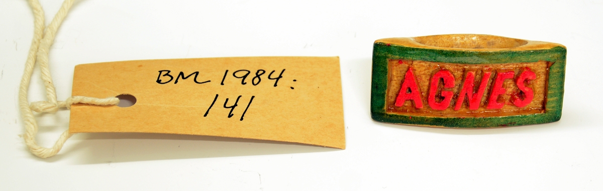 Ring. Fra protokollen: Ring av tre, skåret. Består av et rektangulært felt med bokstaver "AGNES" i relieff, med rødfargede bokstaver og grønn ramme. På baksiden skrevet med tusj "19 GR 44". Lakkert.