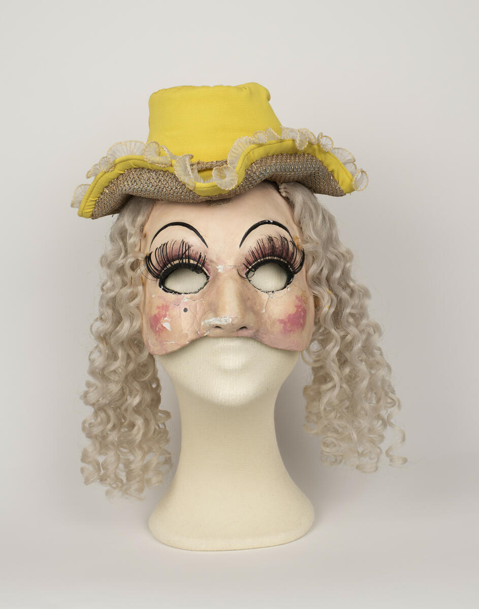 Dubbelmask med hatt och hår använd för rollen "Baronessan" i uppsättningen ”Pierrot i parken”.
Masken består av en halvmask som bärs över ansiktet och en ansiktsmask som bärs över bakhuvudet. Hatten och håret sitter fast i masken.