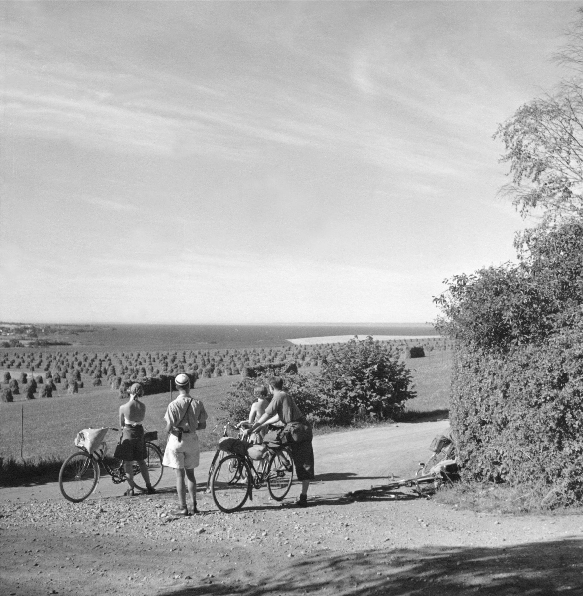 Cyklister tar paus i en grusvägkorsning på Östgötaslätten. Utsikt över ett landskap med åkrar och vatten.