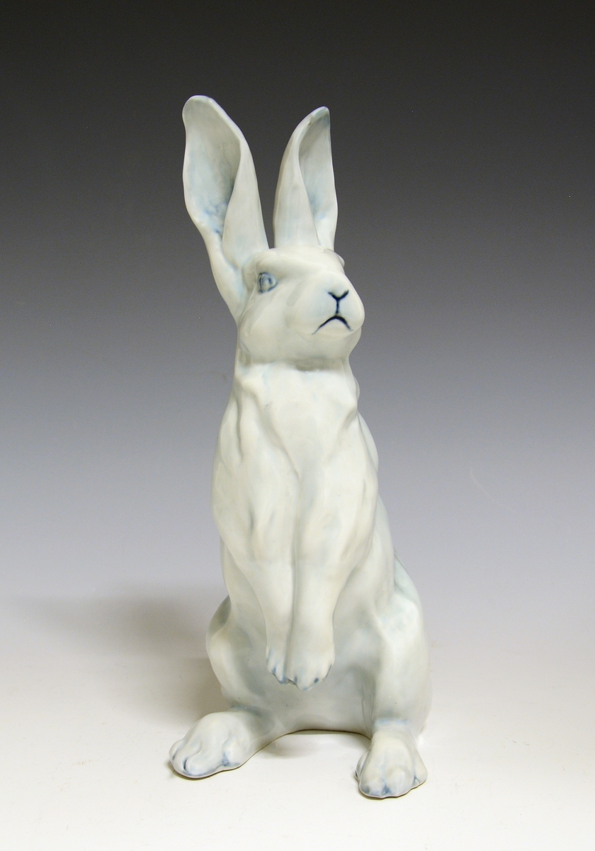 Prot: Figur av porselen. Hare sittende på bakbena. Blågrå farger, glasert (underlagsfarge). Design: Sirnes, prod. 1910.
Modellnr: 1952