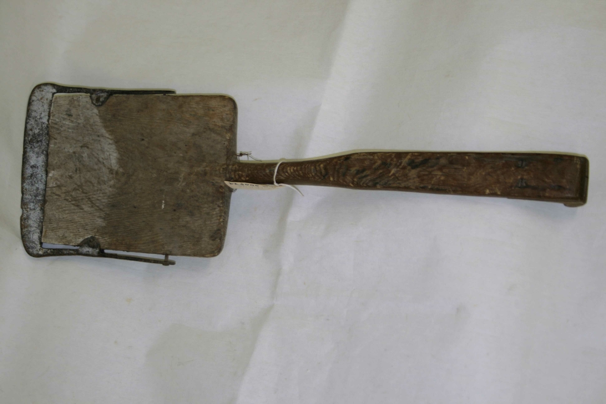 Liten jernskodd spade i tre med kort skaft, spadebladet er flat rektangulær, laget i ett sammenhengende trestykke, øverst på håndtaket forsterket.