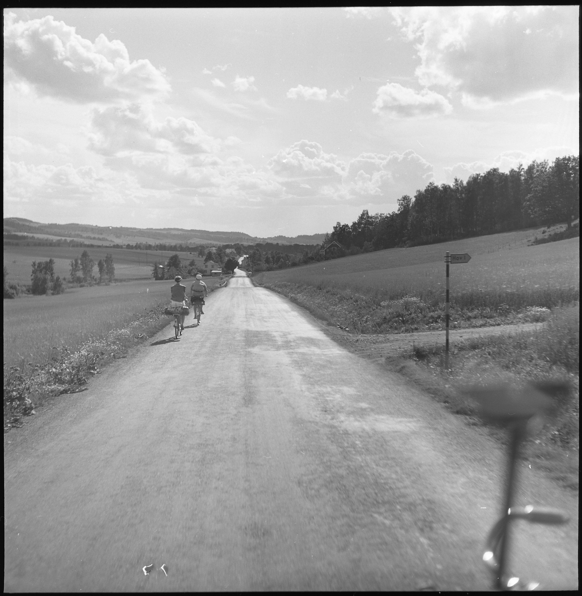 Man och kvinna cyklar på väg i okänt landskap, Troligen ej Alingsåstrakten.