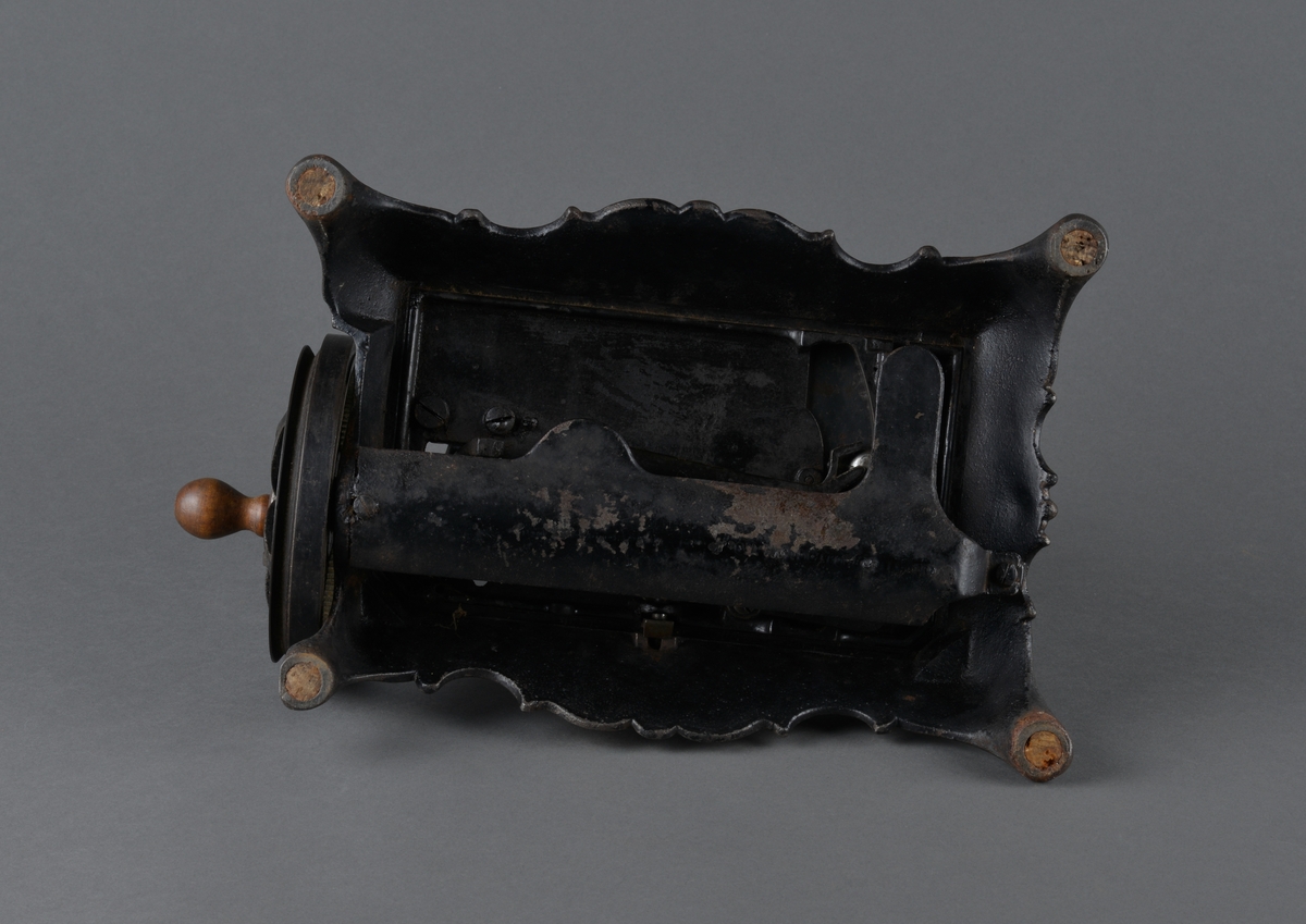 Symaskin med sveiv i svart jern. Den er festet med to hensgler på en solid sokkel av i støpejern.
Sokkelen er rikt dekorert. 

Muligens produsert av GROVEN & BAKER (Boston, USA), produsenter siden 1851.