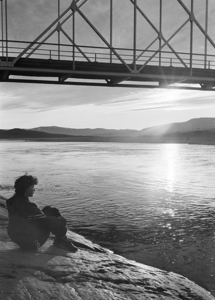Foto av kvinne som sitter ved elva i solnedgang.