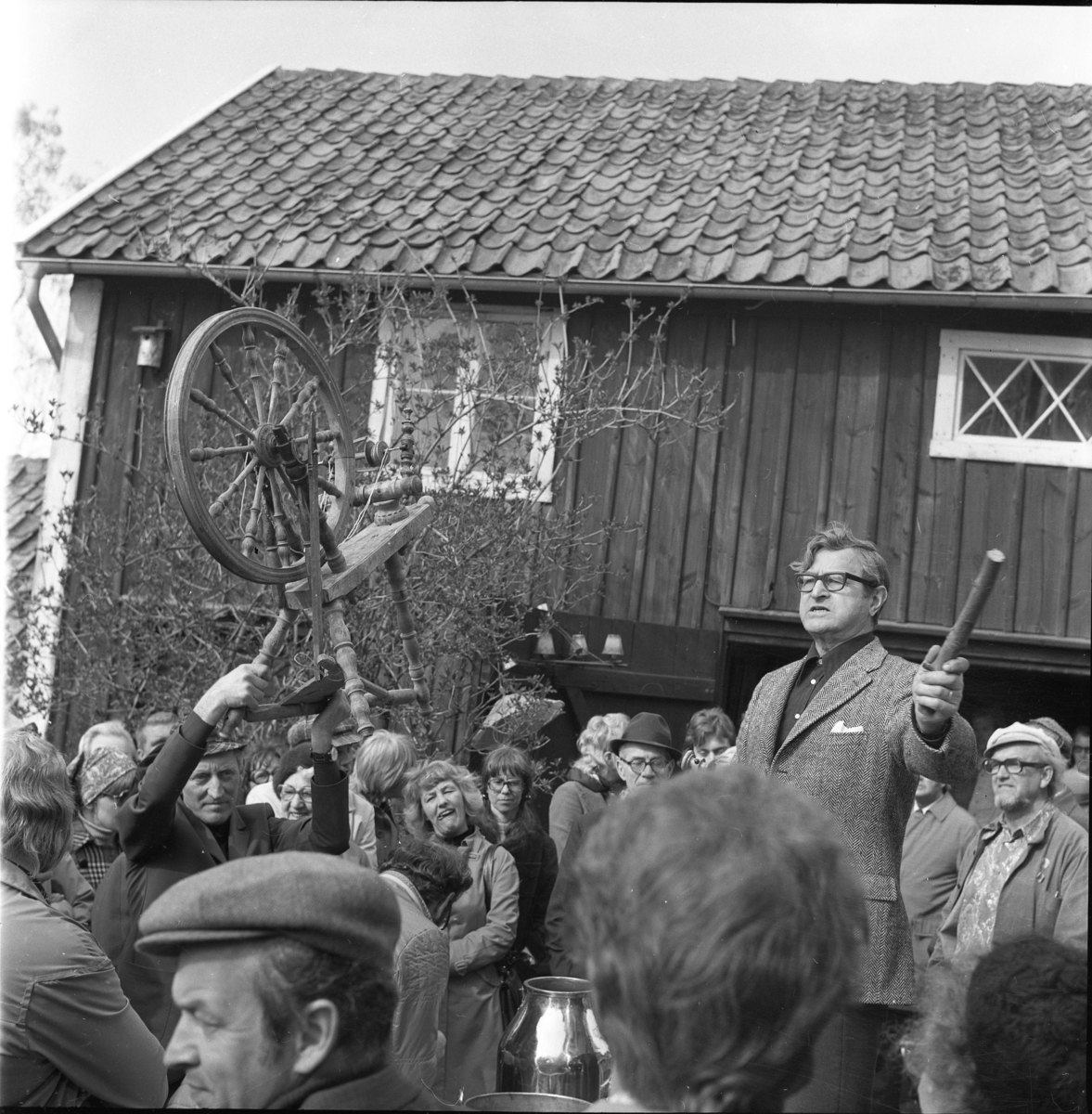 Auktionsutroparen John Karlsson i en folksamling. En man till vänster - Hans Larsson - håller upp en spinnrock.