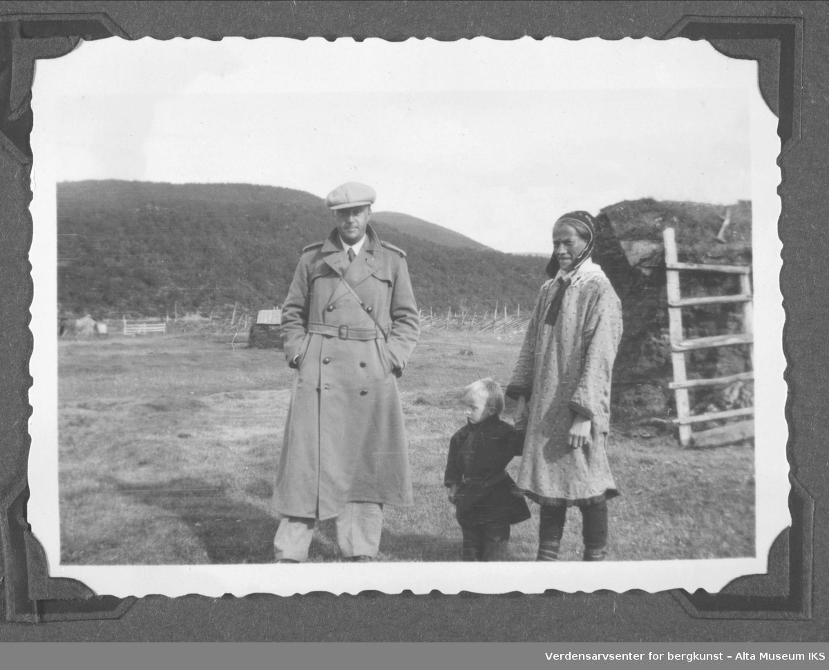 Mann i frakk, kvinne og liten gutt i kofte, foran gamme