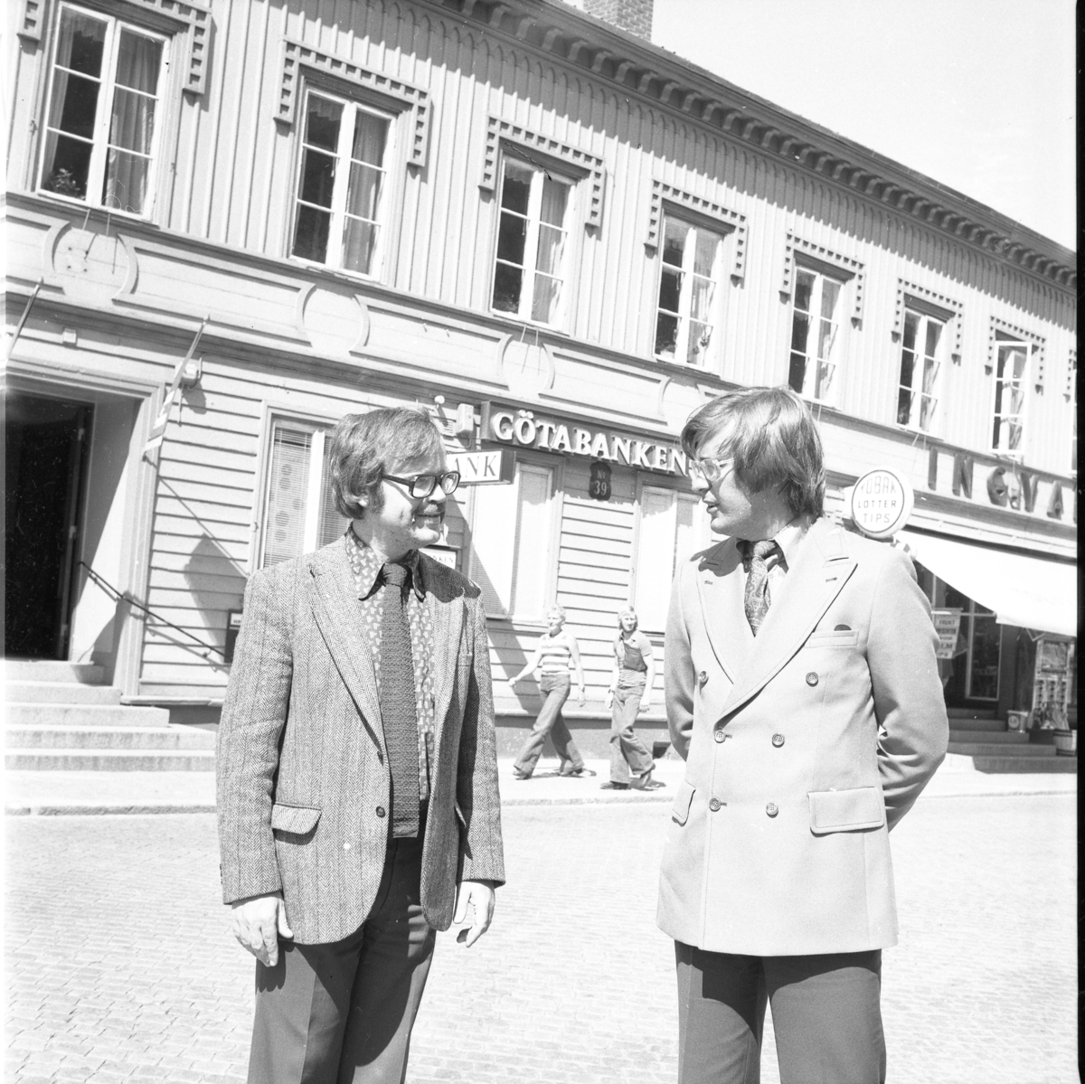 Två män med slips och blazer står vid Brahegatan framför Götabanken i Gränna.