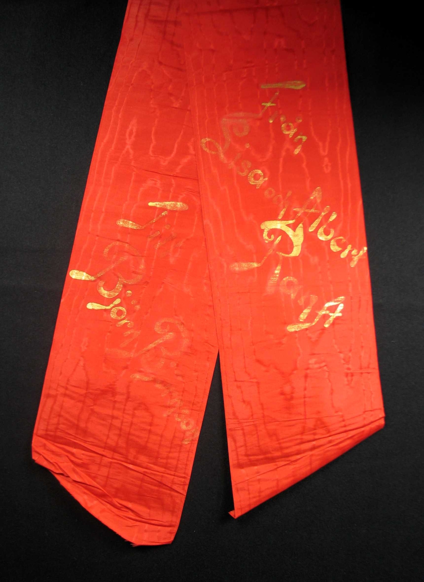Begravelsessløyfe i rød mønstret silke med tekst i gull.