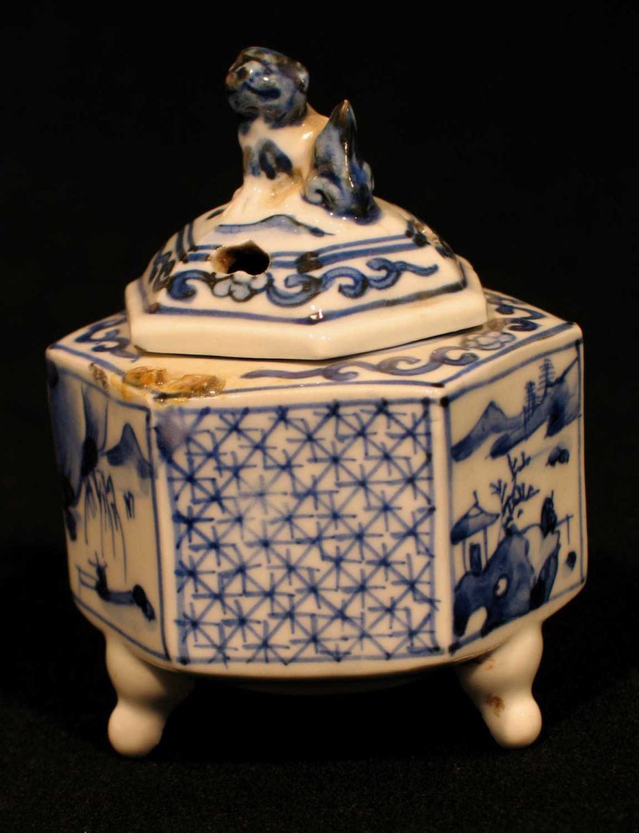 Sekskantet røkelseskar i porselen med tre små bein, hvit underglasur og blå overglasur. Karet er sekskantet der felter er dekorert med landskap og kryssmønster. Hundefigur på toppen.