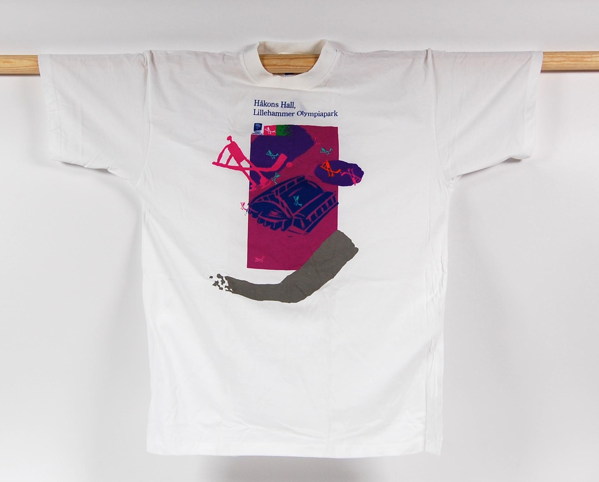 Hvit t-skjorte med flerfarget motiv. Motivet er av Håkons Hall på Lillehammer og piktogrammer av ishockeyspillere. På t-skjorten er det også en logo for de olympiske vinterleker på Lillehammer i 1994. T-skjorten er i størrelse L.