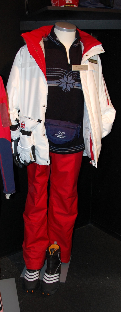 Vinterdress bestående av hvit jakke og rød bukse. På jakken er det festet et merke med motiv av det norske flagget og de olympiske ringene. Jakken har hette med pelskant.