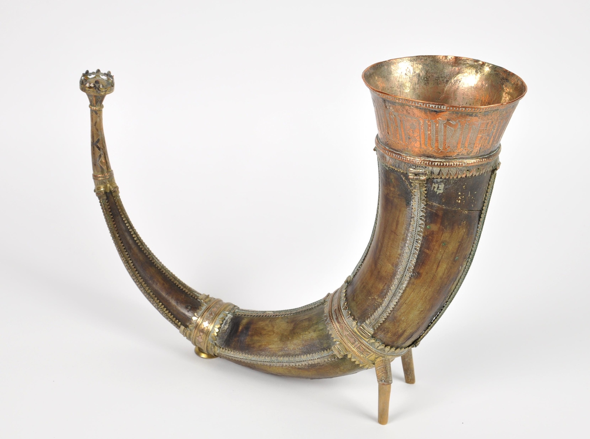 Drikkehorn med metallbeslag rundt kanten, to ringer rundt hornet, et beslag på spissen og smale langsgående beslag. Den største ringen har fester for støttebein. De nåværende beina er ikke de opprinnelige. Beslagene er av forgylt bronse. Krone i spissen. Graverte beslag med geometriske border.