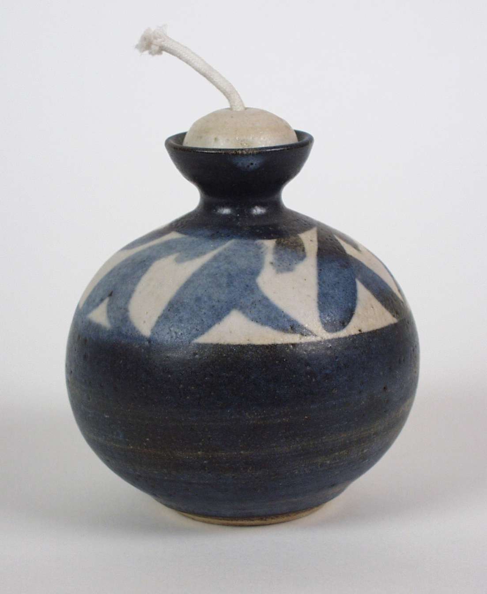 Kuleformet oljelampe i keramikk med enkel strekdekor øverst.