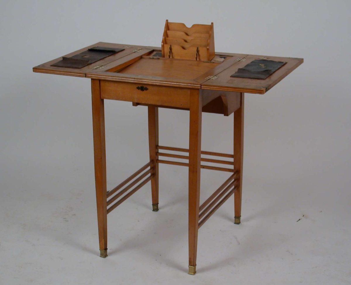 Et lite, firkantet sekretærbord med utbtrettbar skriveplate og brevholder. Platen og bena er av bjørkefiner.