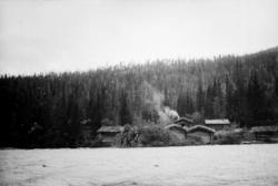 Landskap, tømmerhus, ved vannkanten tre fiskere