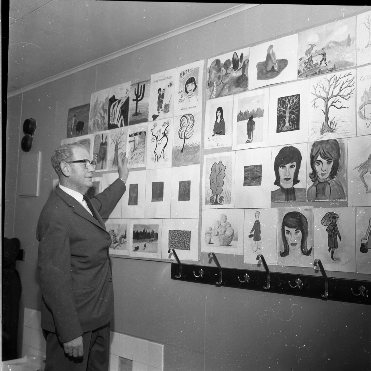 Flera teckningar täcker en vägg. En man står och gestikulerar framför väggen som om han visar och pratar om konsten.