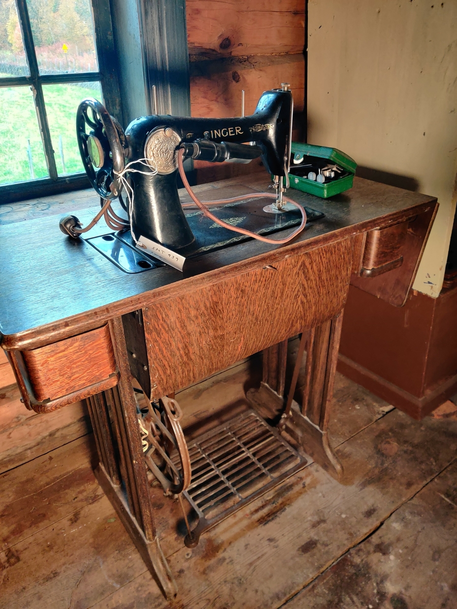 Trådrevet symaskin på stativ med elektrisk arbeidslampe og utfellbart bord og skuffer.